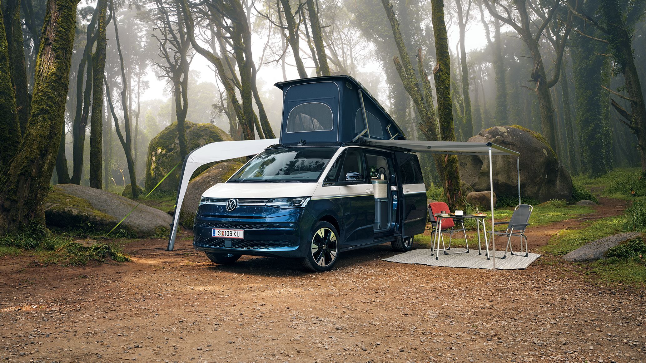 New California steht mit ausgeklapptem Dach und ausgefahrener Marquise in einem Wald, Campingstühle stehen unter der Marquise